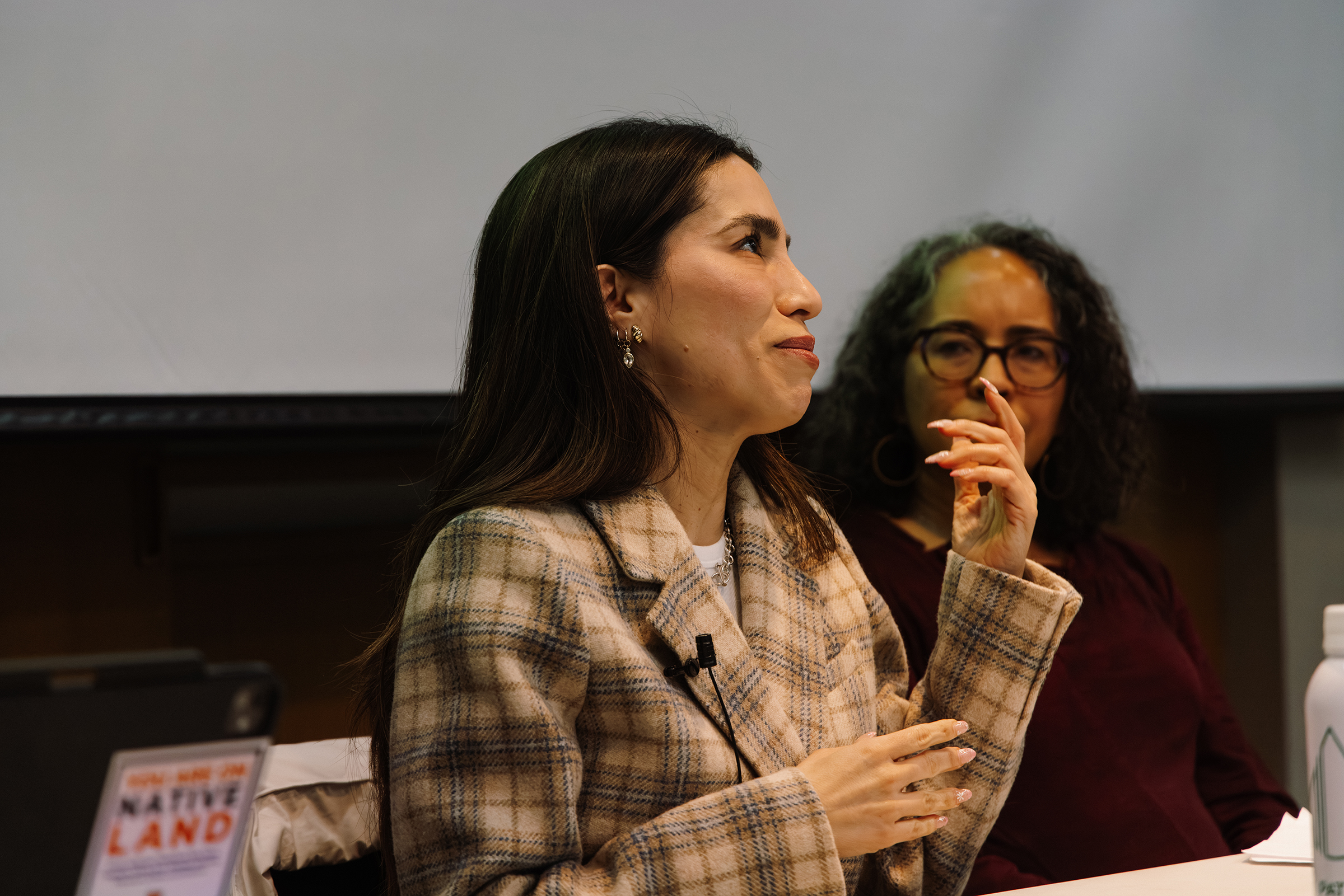 Stephanie Canizales looks to the ceiling in thought, raising a hand, as she sits on a panel.