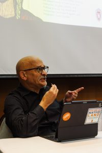 Gilberto Rosas points, looks to the ceiling, and speaks on a panel. 